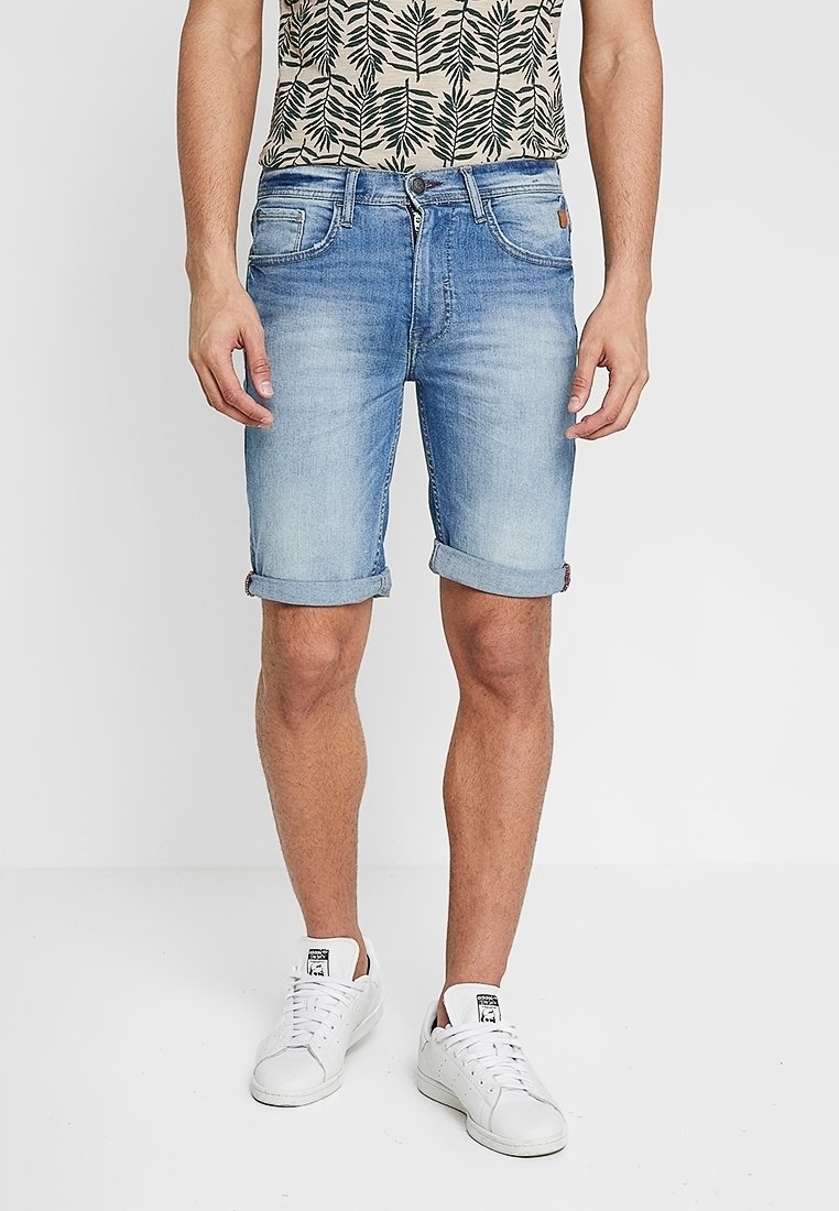 Ljusblå denimshorts med upprullade fållar, utrustade med fem fickor och en kontrasterande logga. Bärs tillsammans med en mönstrad kortärmad skjorta.