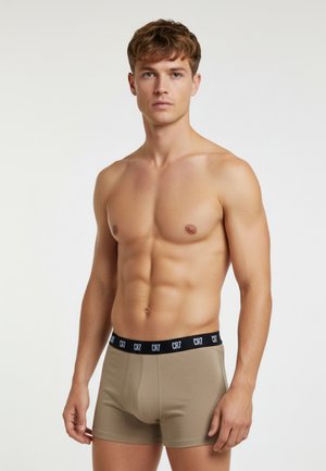 Beige Boxershorts mit einem schwarzen elastischen Bund, der das "CR7"-Logo zeigt. Glatter Stoff und figurbetontes Design, getragen von einem männlichen Modell.
