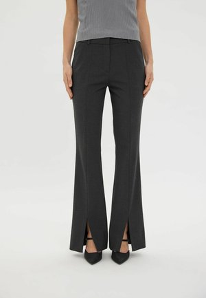 Mujer con pantalones de campana gris carbón con aberturas delanteras, combinados con tacones negros de punta fina y un top gris acanalado.