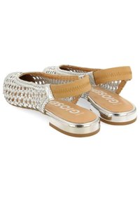 Sandales tressées argentées avec une sangle beige, talon plat en métal et semelle intérieure marron arborant un texte logo blanc. Design ouvert pour une meilleure respirabilité.