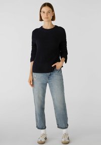 Marineblauer gerippter Pullover mit rundem Ausschnitt, langen Ärmeln und seitlichen Schlitzen, kombiniert mit hellblauen, ausgewaschenen Jeans und cremefarbenen Sneakern.