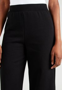Zwarte high-waisted broek met een geribbeld tailleband, gemaakt van een zachte, getextureerde stof, met een losse pasvorm en zonder zichtbare patronen of hardware.