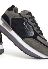Sneakers sportivi con punta in pelle nera texture, corpo in suede grigio e accenti neri. Presentano una suola intermedia bianca e una suola ondulata.