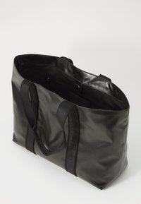 Sacola tote preta feita de material brilhante com duas alças pretas resistentes. O interior possui um revestimento suave e um pequeno bolso com zíper.
