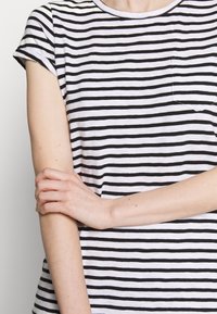 T-shirt à rayures noires et blanches avec des manches courtes, un col rond et une petite poche sur la poitrine. Matière en coton doux, coupe décontractée.