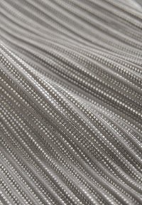 Tissu métallique avec une surface texturée, présentant des rayures verticales et de petits points réfléchissants dans des nuances d'argent et de gris.
