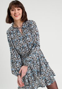 Robe florale noire avec des fleurs bleues et blanches. Présente une taille froncée, des manches ballon et un détail de décolleté en forme de clef. Tissu léger.