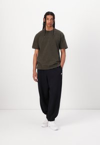 Tricou verde măsliniu, material moale, croială lejeră; pantaloni de trening bleumarin cu glezne strâmte; adidași albi cu talpă texturată; brand discret.