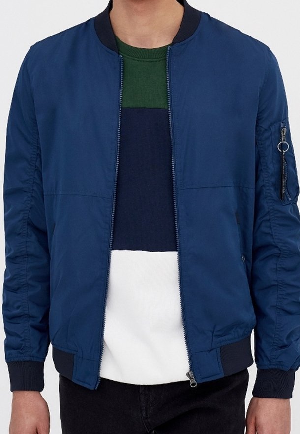 Námořnická modrá bomber bunda s hladkým povrchem, žebrovaným límcem a manžetami, bočními kapsami a kapsou na zip na rukávu pro další detail.