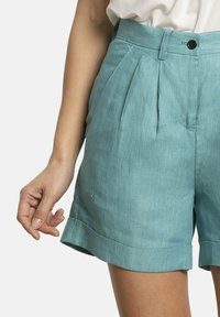 Pantalones cortos de talle alto en azul claro de tejido texturizado, con pliegues, cierre de un botón y dobladillos enrollados.