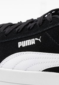Černé semišové tenisky s bílými koženými akcenty, s plochými černými tkaničkami a výrazným bílým logem "PUMA" na boku.
