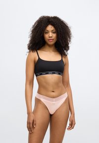 Zwarte bralette met dunne bandjes en een elastische band met merkopdruk. Lichtroze string met kanten rand en een strikaccent aan de voorkant in het midden.