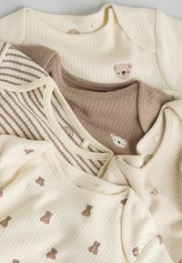 Set de cămăși pentru bebeluși în tonuri crem și maro deschis. Caracteristici includ textură nervurată, dungi orizontale și motive brodate cu ursuleți.