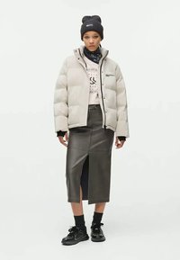 Casaco puffer cinza claro, saia de pele com fenda lateral, boné preto, sweatshirt gráfica e sapatilhas pretas com solas grossas.