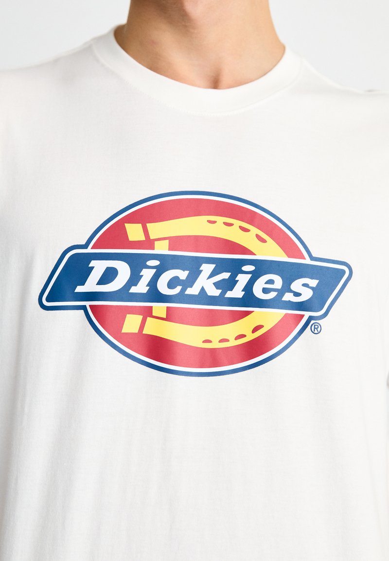 Weißes Baumwoll-T-Shirt mit einem bunten grafischen Logo auf rotem Hintergrund, blauem Banner und gelben Akzenten. Klassisches Rundhals-Design.