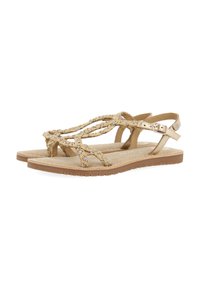 Sandalias beige con tiras trenzadas que presentan detalles metálicos. La suela es plana y texturizada para mayor adherencia. Cierre de hebilla en la tira del tobillo.