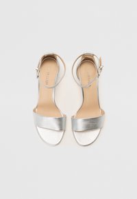 Sølv metalliske hælede sandaler med en bred frontrem, ankelrem med spænde og glat læderoverflade. Flad sål, åben tå-design.