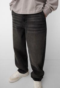 Mustat farkut rentoa leikkausta, joissa on näkyviä etusaumadetaileja ja hieman kuluneita alueita. Yhdistetty valkoisiin lenkkikenkiin.