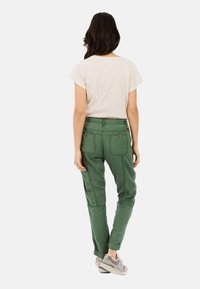 Groene cargobroek met zijzakken, gestyled met een lichtgetextureerd bovenstuk met korte mouwen, gecombineerd met grijze sneakers. Glad materiaal met een ontspannen pasvorm.