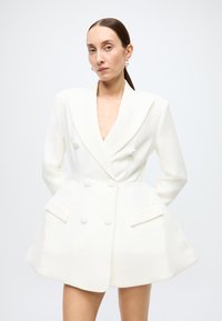White double-breasted blazer with notched lapels, large buttons, and patch pockets, featuring a tailored silhouette and smooth texture.