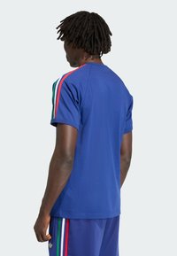 Modré športové tričko z mäkkej látky, s viacfarebnými vertikálnymi pruhmi (zelená, červená) na ramenách a voľným strihom.