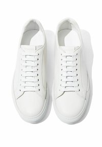 Des baskets en cuir blanc présentent une surface lisse, un design classique à lacets et une semelle en caoutchouc avec une texture subtile. Style minimaliste sans accents.