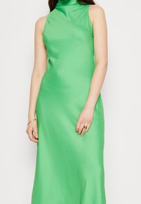 Zielona sukienka bez rękawów z wysokim dekoltem, wykonana z gładkiej tkaniny. Krój dopasowany, długość do kostek.