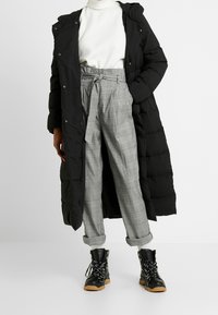 Black puffer coat with a hood, white turtleneck, gray plaid trousers with a tie waist, and black lace-up ankle boots with a chunky sole.