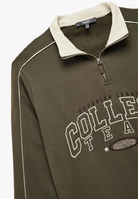 Sudadera de cremallera verde oliva con un cuello beige, ribete blanco y texto impreso "CAMPEONATO DEL EQUIPO UNIVERSITARIO" en morado oscuro. Textura suave.