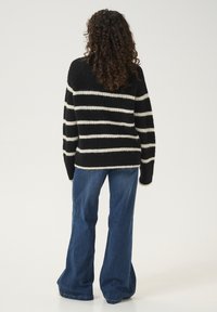 Juodas ir kremas juostuotas per didelis megztinis su tekstūruotu audiniu. Derinamas su platėjančiomis mėlynomis džinsinėmis kelnėmis. Žiūrima iš nugaros.