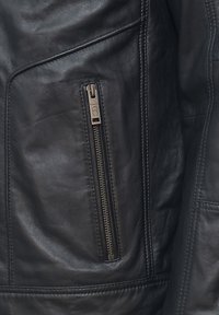 Svart läderjacka med en dragkedjeficka, slät yta och sydda detaljer längs sömmarna. Hållbar metaldragkedja som accent.