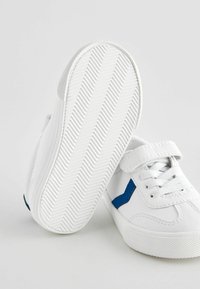 Baskets blanches avec une semelle en caoutchouc texturé et des accents bleus. Elles possèdent une bande auto-adhésive et des lacets. Matériau lisse, design à bout rond.