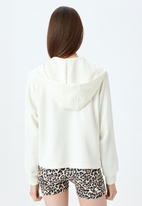 Afgeknotte crèmekleurige hoodie met een trekkoordkap, zachte textuur; gecombineerd met short met luipaardprint en zwart-bruin patronen.