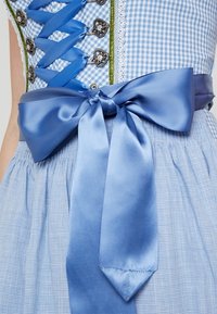 Robe en vichy bleu avec un corsage ajusté, des pièces métalliques en argent ouvragé, des accents verts et un grand nœud en satin à la taille. Tissu texturé.