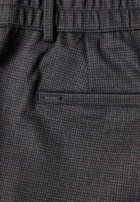 Tissu gris foncé avec un petit motif à carreaux, doté d'une boucle de ceinture et d'une poche arrière horizontale avec une petite étiquette de marque en métal.