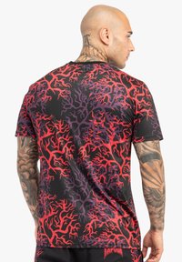 Kortærmet t-shirt med et livligt mønster af grene i sort, rød og lilla, lavet af glat stof med en normal pasform.