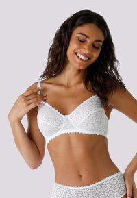 Parte superiore in pizzo bianco a forma triangolare, con bordi ondulati e spalline regolabili decorate con intricati motivi floreali. Tessuto liscio in tutto il capo.