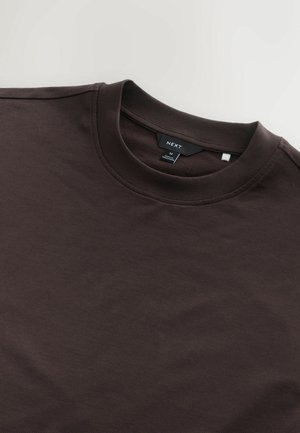 Hnědé tričko s krátkým rukávem vyrobené z bavlny, se žebrovaným kulatým výstřihem a štítkem s nápisem "NEXT." Hladký povrch, minimalistický design.