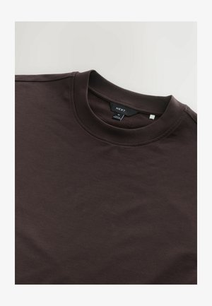 Hnedé tričko s krátkym rukávom vyrobené z bavlny, s rebrovaným okrúhlym výstrihom a štítkom označeným "NEXT." Hladká textúra, minimalistický dizajn.