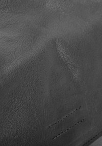 Texture de cuir noir avec un grain fin, montrant des plis et un subtil éclat. Présente des coutures discrètes, soulignant la qualité du matériau.