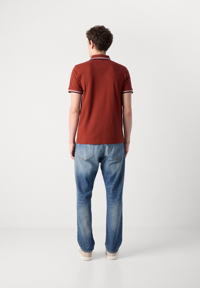 Polo shirt en coton rouge avec col à rayures blanches, associé à un jean en denim bleu clair. Le jean a un design classique à cinq poches.
