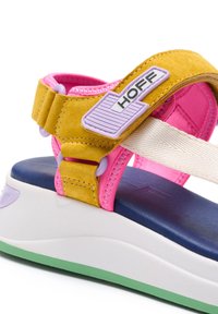 Färgglad sandal med gula mockaband, rosa tygdetaljer och en blå fotbädd. Har en vit mellansula och en grön gummisula.