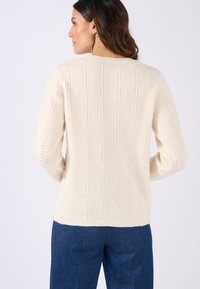 Crèmegekleurde gebreide trui met een verticale ribbelstructuur, open steekdetails, lange mouwen en een ronde halsline.