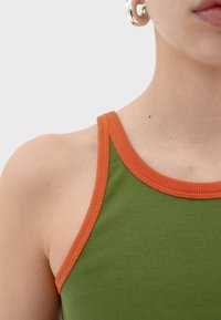 Zelený žebrovaný top bez rukávů s oranžovými detaily; má kulatý výstřih a přiléhavý střih. Hladká textura.