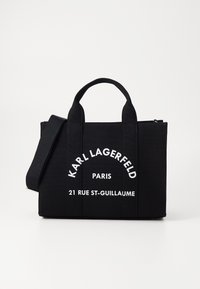 Sort lærredsnettaske med to håndtag og en aftagelig skulderrem. Har hvid tekst: "KARL LAGERFELD PARIS 21 RUE ST-GUILLAUME."