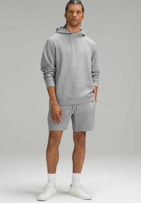 Szara bluza z kapturem o teksturowanej tkaninie i przedniej kieszeni, w zestawie z szarymi szortami. Białe sneakersy i skarpetki za kostkę dopełniają stylizację.