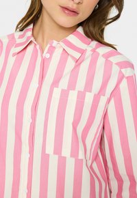 Striped button-up shirt in light pink and cream, featuring a classic collar, a chest pocket, and a relaxed fit with a smooth texture.