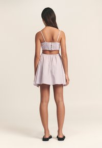 Lila ja valkoisilla raidoilla varustettu kahden osan asu, jossa on rypytetty crop-top nappikiinnityksellä ja flare-mallinen mini-hame. Kangas on kevyt ja sileä.