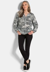 Langärmlige Bluse aus schwarz-weiß gemustertem Stoff, V-Ausschnitt, kombiniert mit schwarzen Skinny-Jeans und schwarzen Sneakers mit weißen Sohlen.