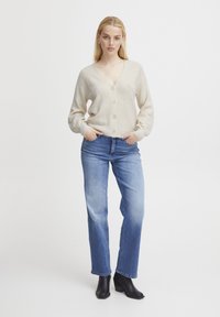 Beige knit cardigan with a V-neck, five buttons, and ribbed cuffs, paired with light blue straight-leg jeans and black heeled ankle boots.